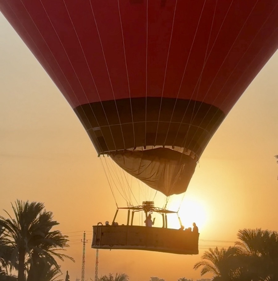 A colorful hot air balloon rising over the Valley of the Kings in Luxor, Egypt, during sunrise.
