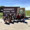 A happy group of international travelers posing together in front of the official Serengeti National Park entrance sign during a Gagago tour.