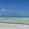 Colorful kitesurfing kites floating above the shallow turquoise water at Paje Beach, Zanzibar.