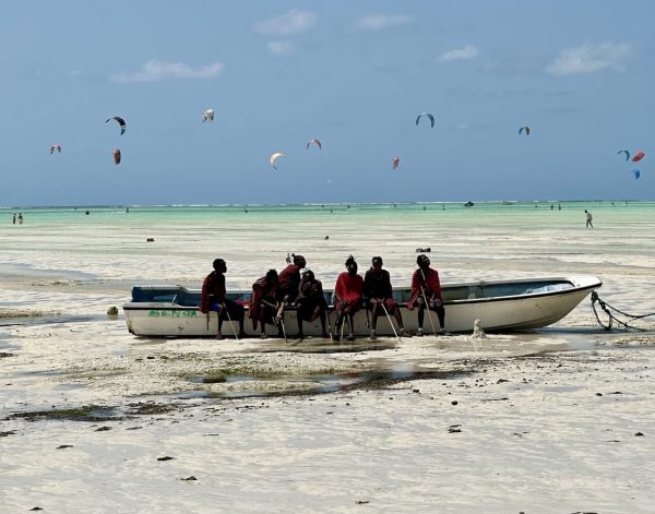 A group of Maasai sitting on a traditional wooden dhow boat in the turquoise lagoon of Paje Beach, Zanzibar.