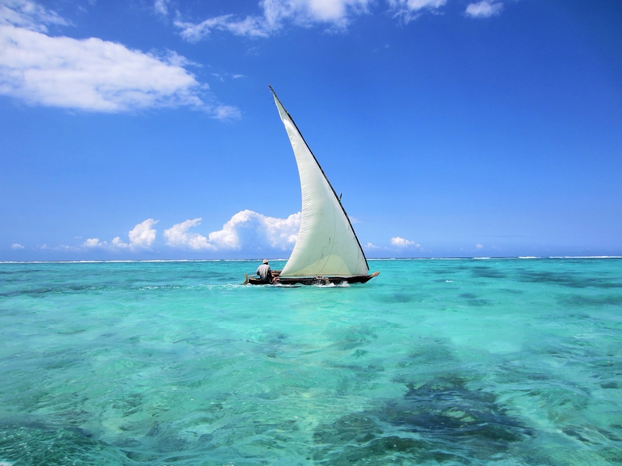 Traditional wooden dhow boat sailing on crystal-clear turquoise waters in Zanzibar during a Gagago island tour.