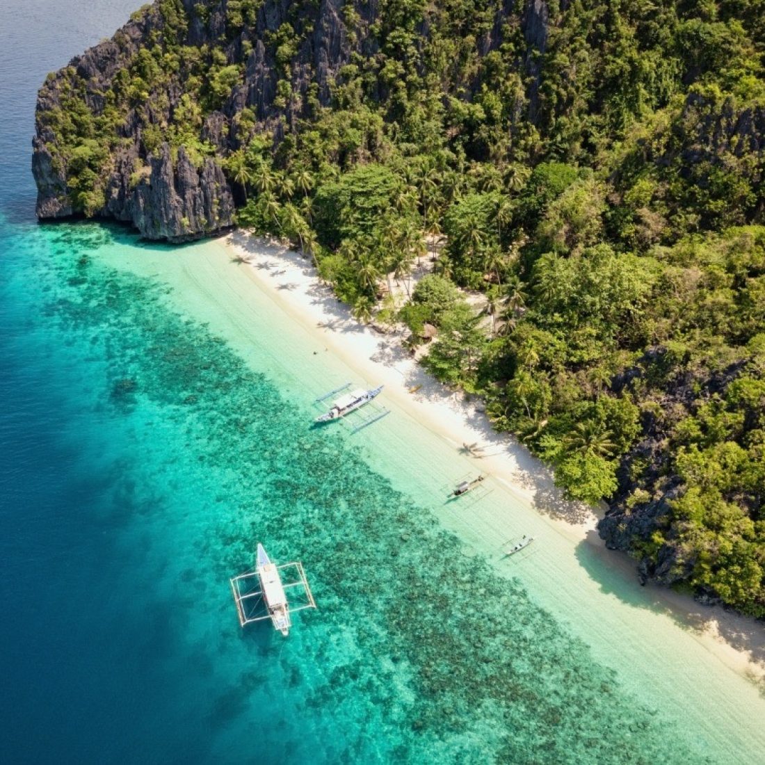Aerial view of a pristine tropical beach in the Philippines with turquoise water and white sand.